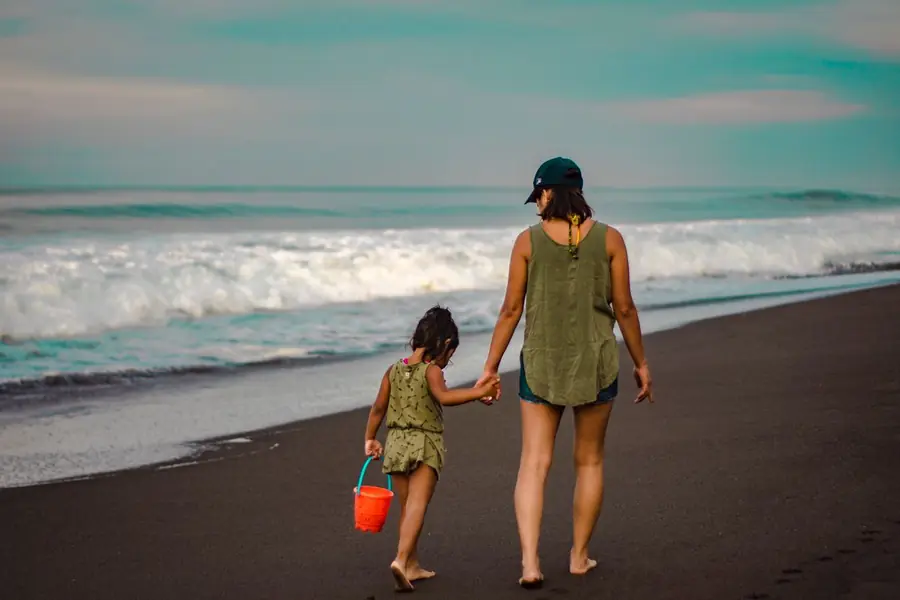 A helper and child walking hand in hand along a Mediterranean beach