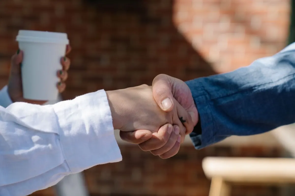 Two people shaking hands outdoors over a coffee