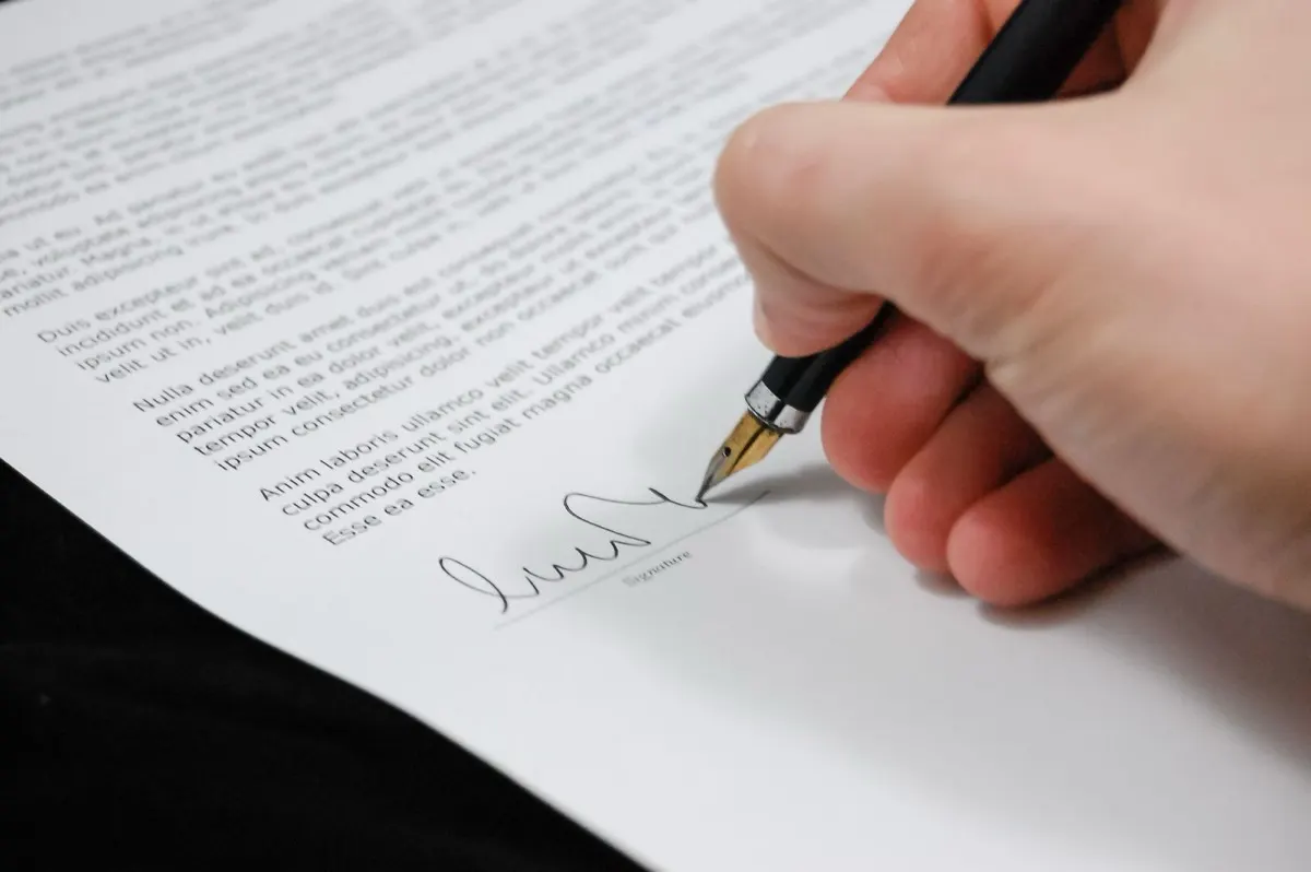 A hand signing a printed employment contract with a pen