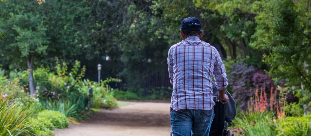 A carer pushing a wheelchair along a leafy garden path