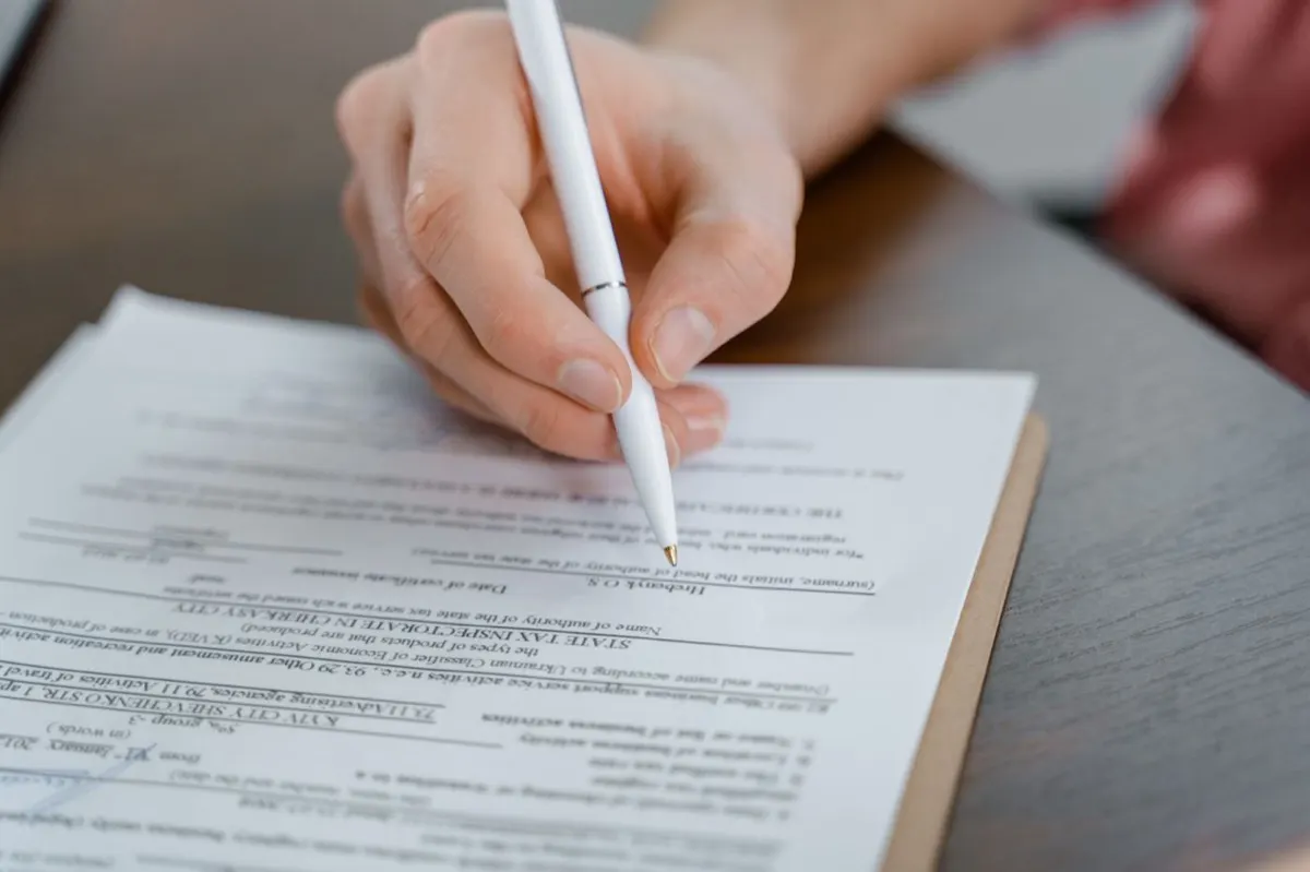 A hand signing the official employment contract at a wooden table