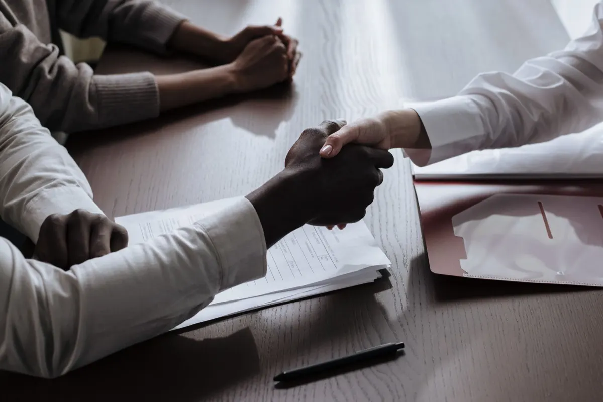 Two people shaking hands across a table at the end of an interview